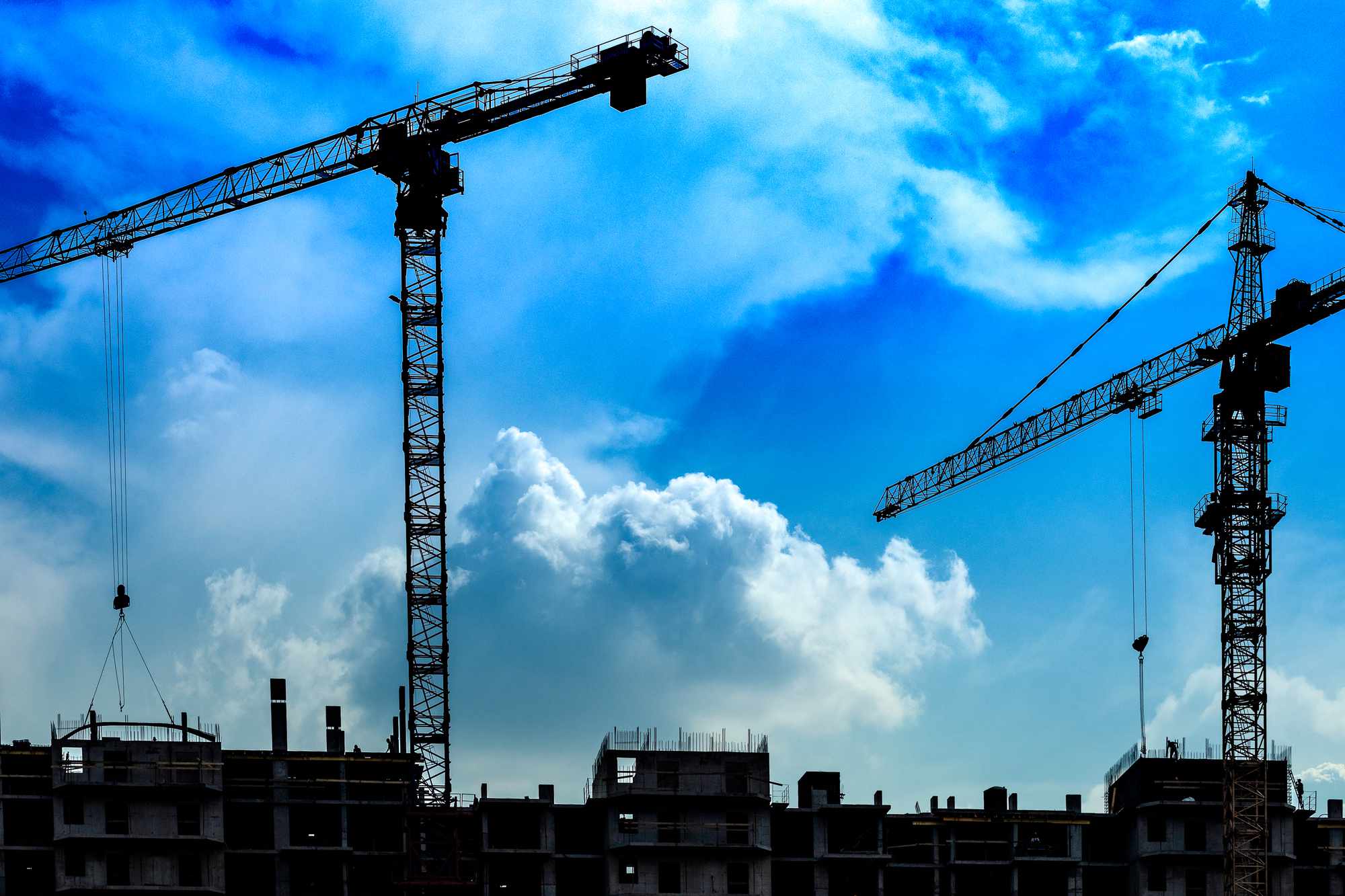 A construction site with two tall cranes and blue sky with white clouds.