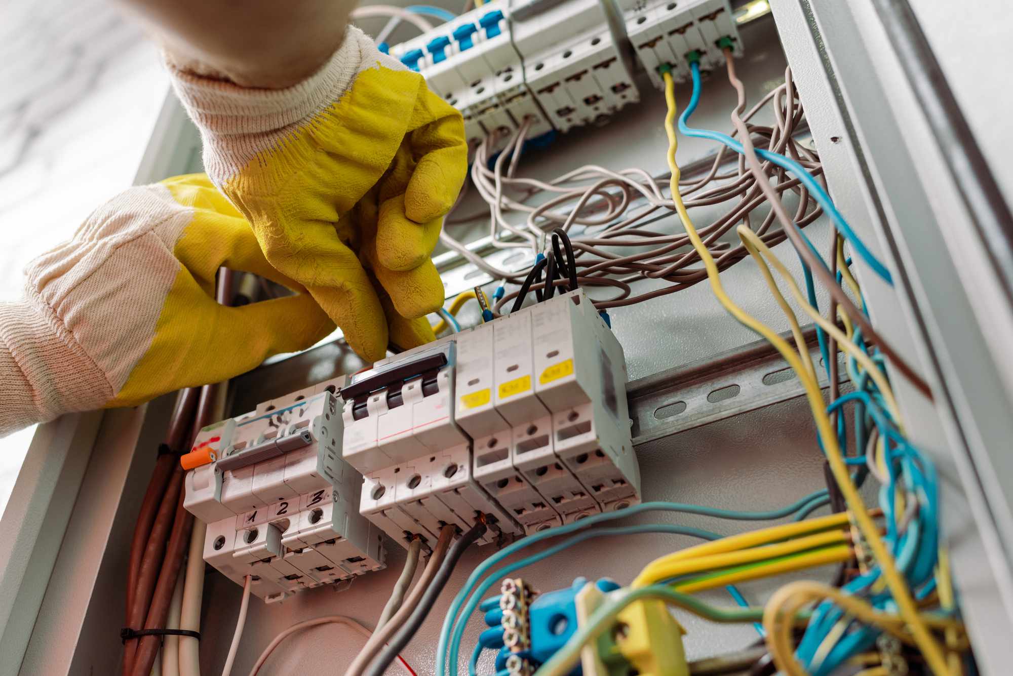 Electrician's hands adjusting an electrical panel from below.