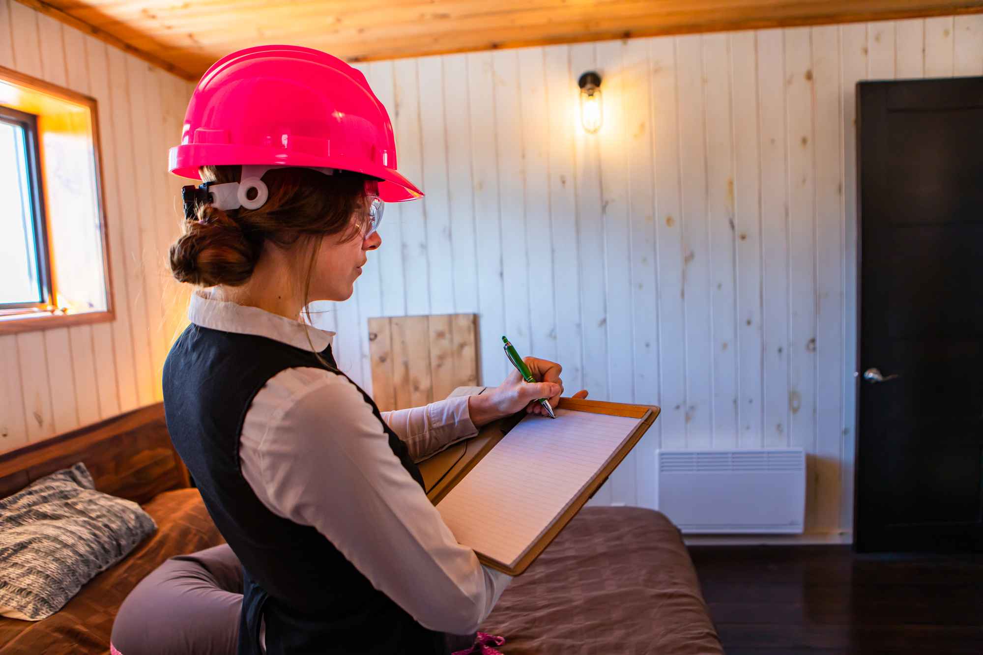 A home inspector in a pink helmet holding a clipboard doing a home inspection.