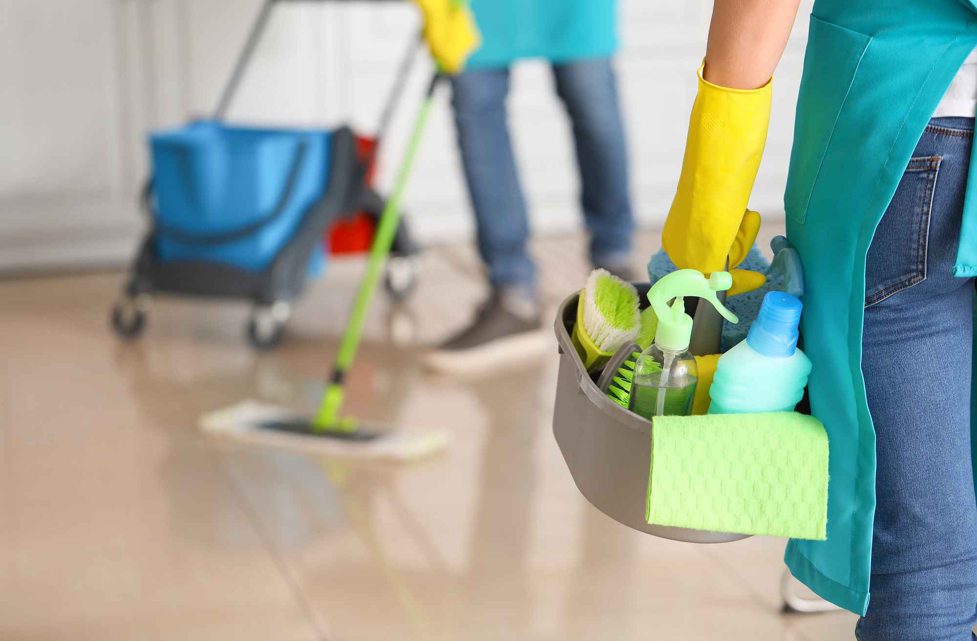 A cleaner holding cleaning supplies in a light green bucket.