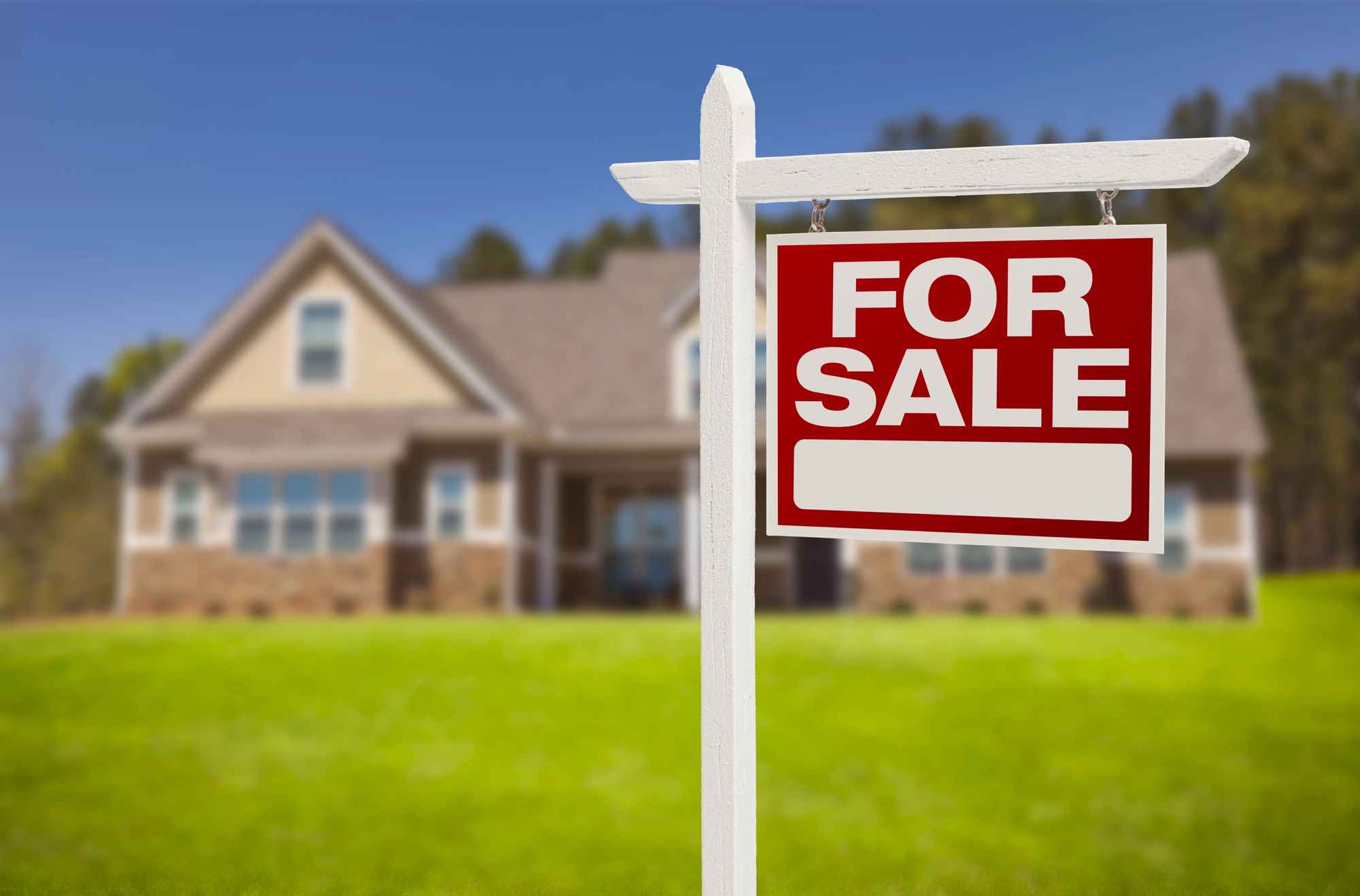 A suburban home with a FOR SALE sign in front.