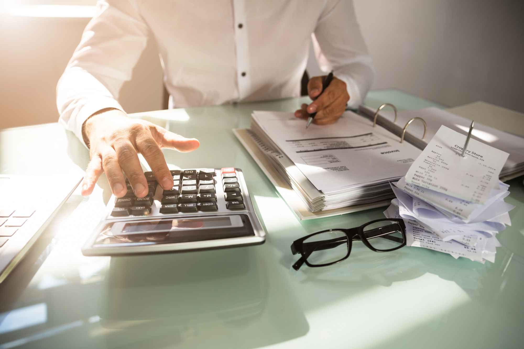 An accountant wearing a white button down crunching numbers on a calculator.