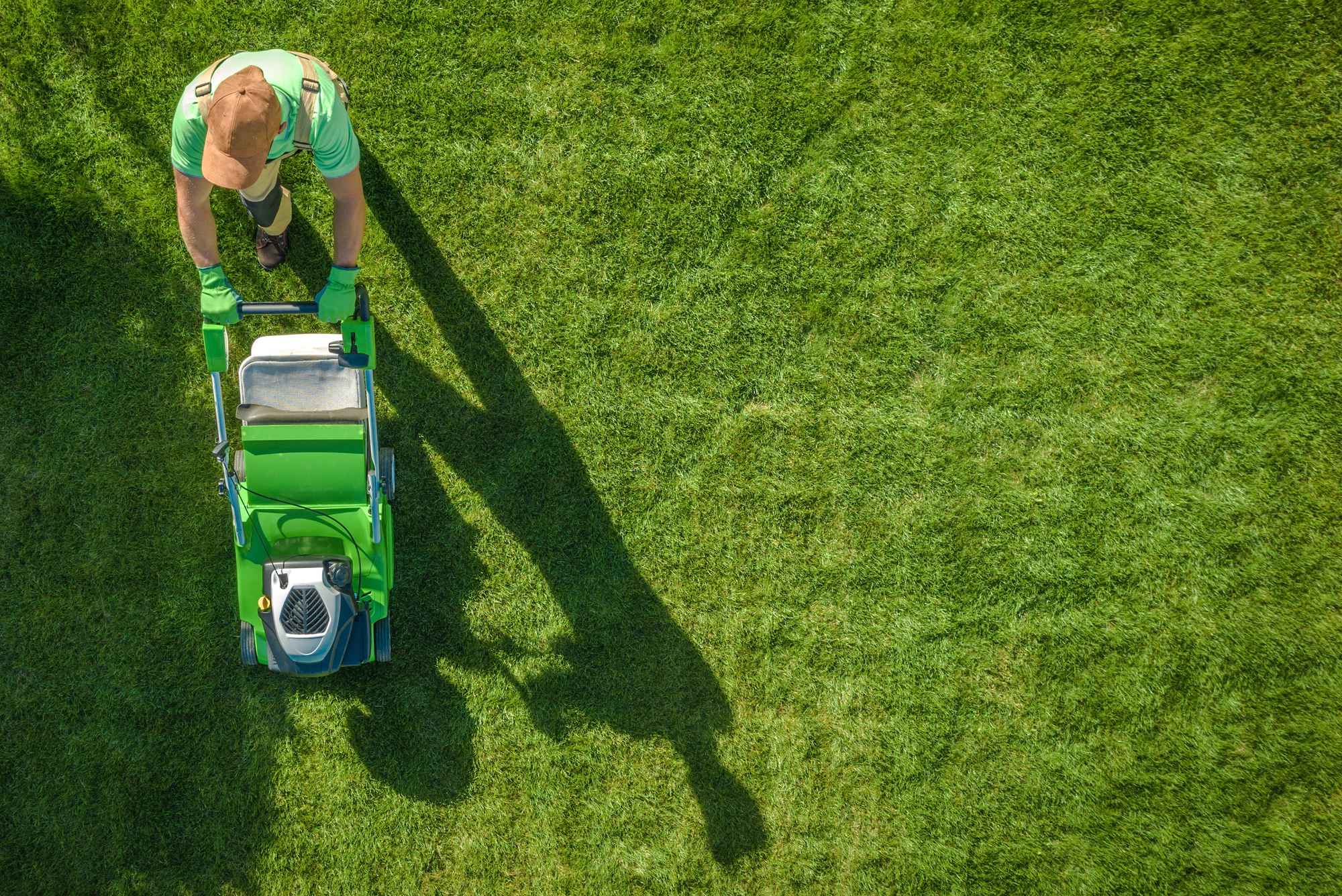 A landscaping worker mowing a lawn from above.