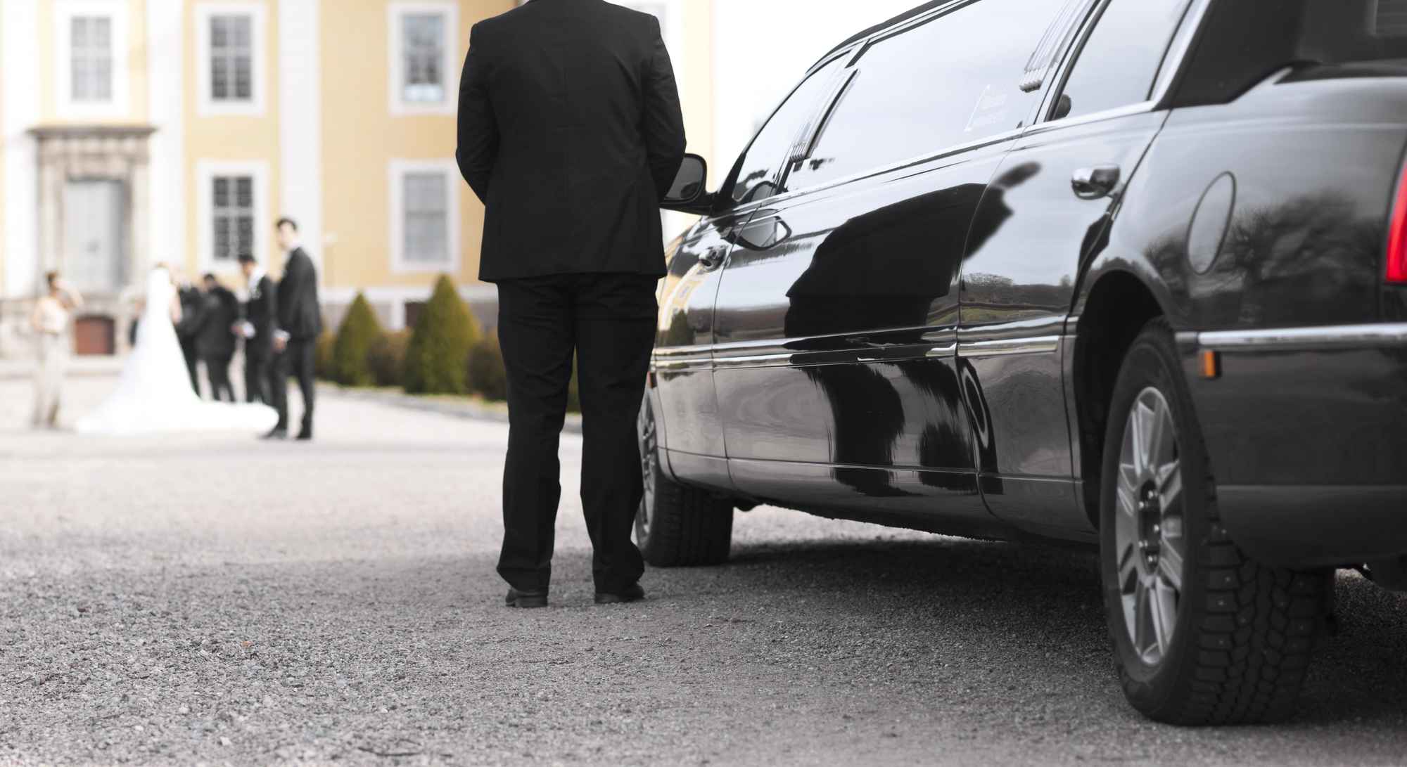 A black limousine and driver parked in front of a wedding venue.