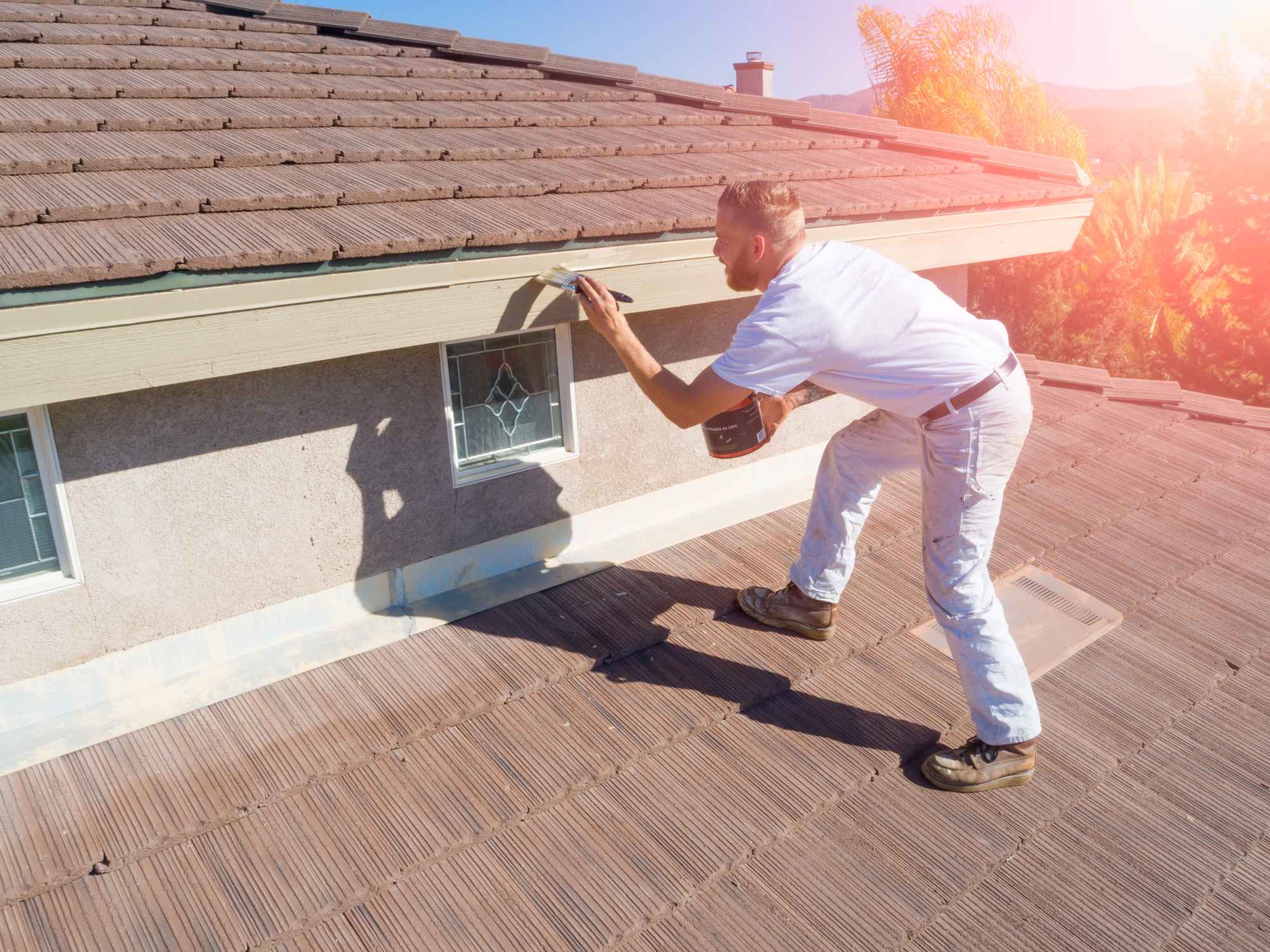 A professional painter wearing white painting trim on a roof on a sunny day.